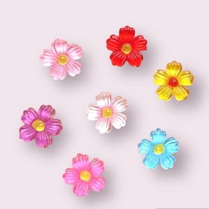 May include: Seven colorful flower-shaped resin embellishments in pink, red, yellow, and blue. The flowers are all the same size and shape, and they have a glossy finish.