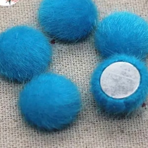 May include: A set of five blue fuzzy pom poms with a white adhesive backing. The pom poms are soft and fluffy and would be great for adding a touch of whimsy to crafts.