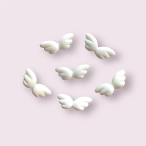 May include: Seven white plastic angel wings, each with a slightly different shape and size.