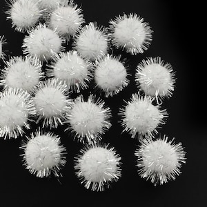 May include: A collection of white pom-poms with silver glitter accents. The pom-poms are scattered on a black background.
