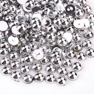 May include: A large pile of silver round-shaped embellishments with a raised center. The embellishments are shiny and have a smooth surface.