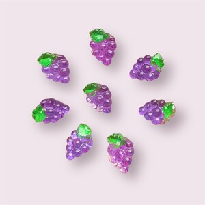 May include: Eight purple grape clusters with green leaves, arranged in a circle on a light pink background.