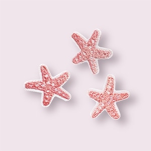 May include: Three embroidered starfish patches in shades of red with white borders. The patches are arranged on a light pink background. These patches are ideal for adding a nautical touch to clothing, bags, or other craft projects.