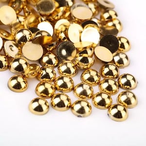 May include: A large pile of gold-colored round metal embellishments with a domed top. The embellishments are scattered on a white surface.