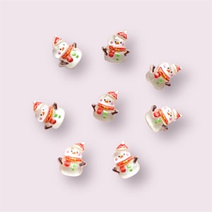 May include: Small, clear snowman figurines with red hats, scarves, and brown twig arms. The snowmen have black dot eyes and orange carrot noses. These festive decorations are perfect for holiday crafts or seasonal displays.