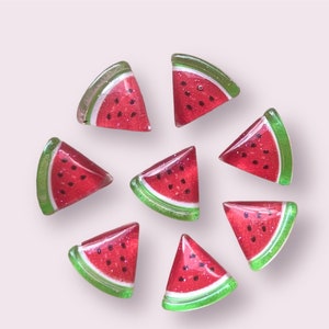 May include: Eight watermelon slice shaped glass cabochons with green edges and red and black watermelon details.