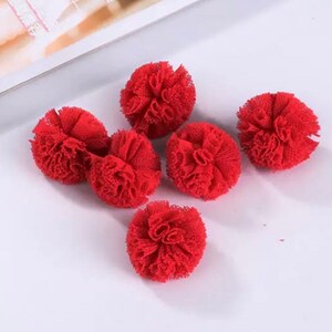 May include: Six red pom-poms made of tulle fabric. The pom-poms are arranged in a cluster on a white surface.