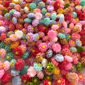 May include: Assortment of colorful resin flower embellishments in various shapes and sizes. The flowers are in shades of pink, blue, green, yellow, and white.
