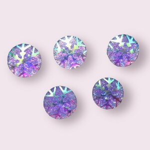 May include: Five iridescent purple snowflake-shaped buttons with a glitter finish.