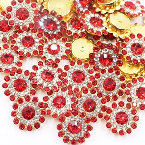 May include: A pile of red and clear rhinestone embellishments with gold settings. The rhinestones are arranged in a flower shape.