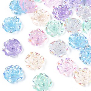 May include: Assortment of iridescent rose-shaped embellishments in various pastel colors, including pink, blue, purple, and green. The embellishments are made of clear plastic and have a 3D rose design.
