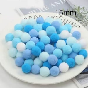 May include: A collection of 15mm blue and white pom poms. The pom poms are arranged in a pile on a white plate.
