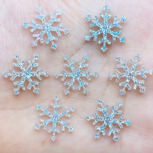 Peut inclure: Six flocons de neige scintillants. Chaque flocon est blanc translucide avec des paillettes irisées, captant la lumière. Ces éléments décoratifs sont parfaits pour l'artisanat, le scrapbooking ou les décorations de fêtes.