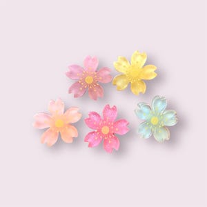 May include: Five pastel-coloured ceramic flower-shaped dishes. The dishes are in shades of pink, yellow, and blue. Each dish has a five-petal flower design with a yellow centre.