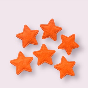 May include: Six orange felt stars on a white background. The stars are all the same size and shape.