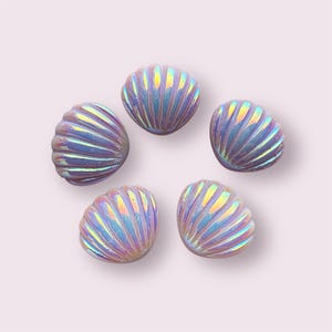 May include: Six iridescent purple seashell shaped buttons. The buttons have a pearlescent finish and are perfect for adding a touch of whimsy to any project.