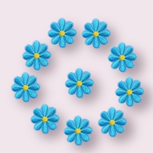 May include: Ten blue felt flower patches with yellow centres. The flowers are arranged in a circle on a white background.
