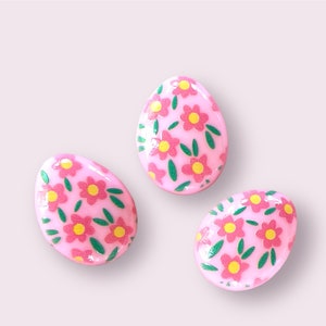 Peut inclure: Trois œufs de Pâques roses avec un motif floral. Les œufs sont décorés de fleurs roses et de feuilles vertes.