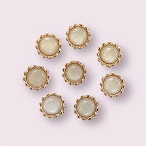 Peut inclure: Huit boutons dorés avec un centre blanc. Les boutons ont un bord festonné.
