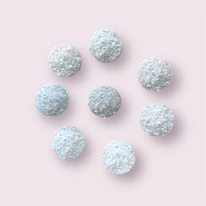 May include: Eight iridescent white round ornaments with a textured surface. The ornaments are arranged in a circle on a light pink background.