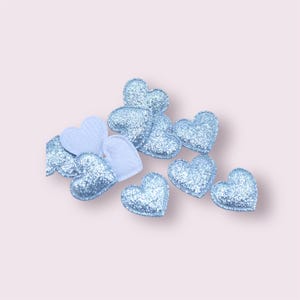 May include: A scattering of light blue glitter heart-shaped embellishments. The hearts are made of a soft, fuzzy material and have a sparkly finish.