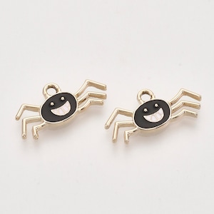 May include: Two gold-coloured spider charms with black enamel bodies and white enamel smiling faces. The spiders have eight legs and are perfect for adding a spooky touch to jewellery or crafts.