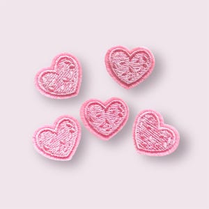 May include: Five pink felt heart-shaped patches with white stitching and a white polka dot pattern.