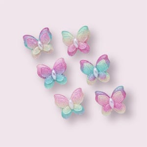 May include: Six iridescent butterfly-shaped embellishments with glitter. The butterflies are in shades of pink, blue, and green.