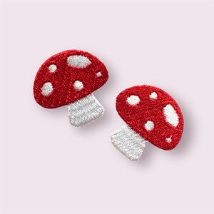 May include: Two embroidered mushroom patches. Each patch has a red cap with white spots and a white stem. The patches are designed with a textured, stitched appearance, ideal for adding to clothing or accessories.