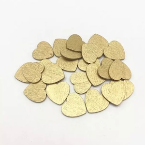 May include: A pile of small, gold-coloured wooden hearts. The hearts are scattered on a white surface.