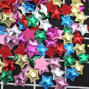 May include: A large assortment of colourful, metallic star-shaped embellishments. The stars are made of a variety of materials, including felt, fabric, and glitter. They are perfect for adding a touch of sparkle to crafts, cards, and other projects.