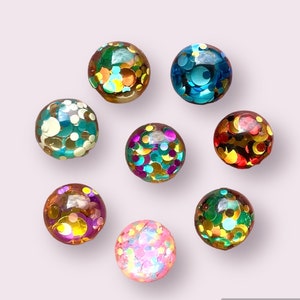 May include: Eight colourful round ornaments with a confetti design. The ornaments are made of glass and have a variety of colours, including blue, green, red, pink, and gold.