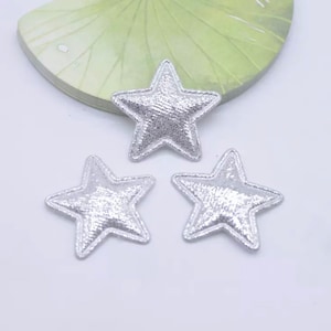 May include: Three silver metallic star-shaped fabric patches. The stars have a slightly raised, textured surface.