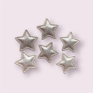 Pode incluir: Seis patches de tecido em forma de estrela com glitter prateado. As estrelas medem aproximadamente 5 cm de di&acirc;metro.