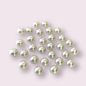 May include: A collection of white pearl beads, scattered on a light purple background.