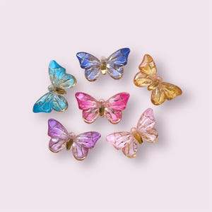May include: Six colourful butterfly-shaped glass beads with gold accents. The beads are in shades of blue, pink, purple, and orange.
