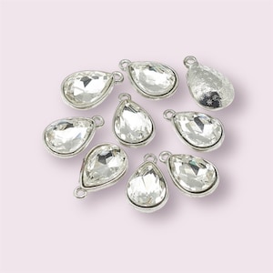 May include: Ten silver teardrop-shaped charms with clear crystal accents. The charms have a loop at the top for attaching to jewellery or other crafts.