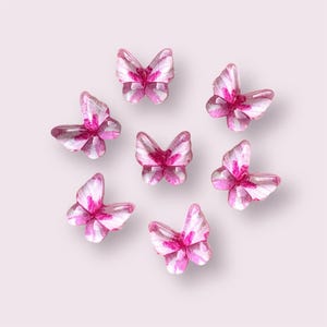 May include: Seven pink and white glass butterfly charms with a glittery finish.