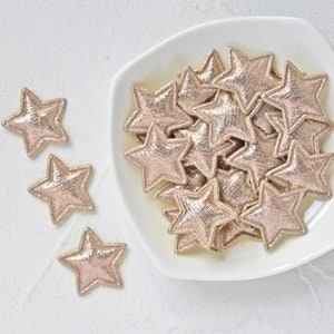 Peut inclure: Un bol blanc rempli de décorations en forme d'étoile dorées à paillettes. Les étoiles sont éparpillées autour du bol et certaines se chevauchent.