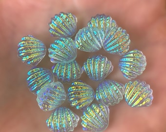 May include: A collection of iridescent seashell-shaped charms in shades of blue and green. The charms are made of glass and have a textured surface.
