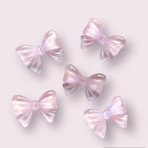 May include: Five iridescent pink bows with a shimmery finish. The bows are arranged in a scattered pattern on a light pink background.