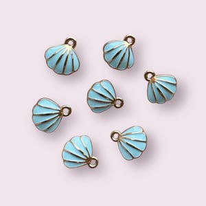 May include: A set of eight gold-toned metal charms shaped like seashells. The shells are painted a light blue colour with gold accents.