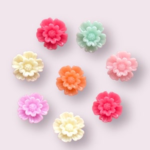 May include: Eight pastel-colored flower-shaped resin cabochons. The colors are pink, light pink, peach, light green, cream, and lavender.