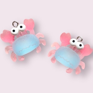 May include: Two small pink and blue plastic crab charms with white eyes and silver jump rings.