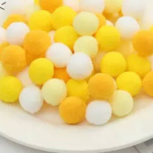 May include: A collection of yellow and white pom poms. The pom poms are soft and fluffy and would be great for crafts or decorations.