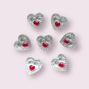 May include: Seven silver heart-shaped embellishments with red rhinestone centers.