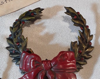 May include: A gold-toned wreath with red berries and a large red bow. The wreath is made of metal and has a rustic look.