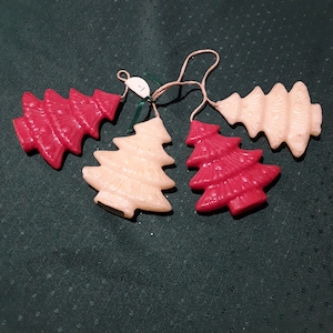 May include: Four Christmas tree ornaments in red and off-white, strung together with twine. The ornaments are arranged on a dark green textured surface. The trees are stylized with a textured surface.