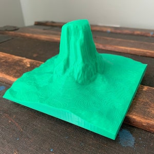 Puede incluir: Un modelo impreso en 3D de una cordillera con un acabado de plástico verde. El modelo está detallado con líneas de contorno y un pico.