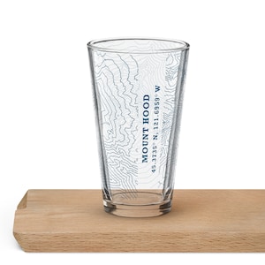 May include: A clear glass with a topographic map design of Mount Hood, Oregon. The text "MOUNT HOOD 45.3735° N, 121.6959° W" is printed on the side of the glass.